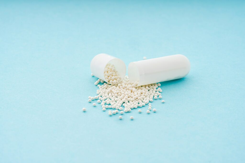 Gel capsule opened. White medicine powder spilled out on light blue background from capsule drug.