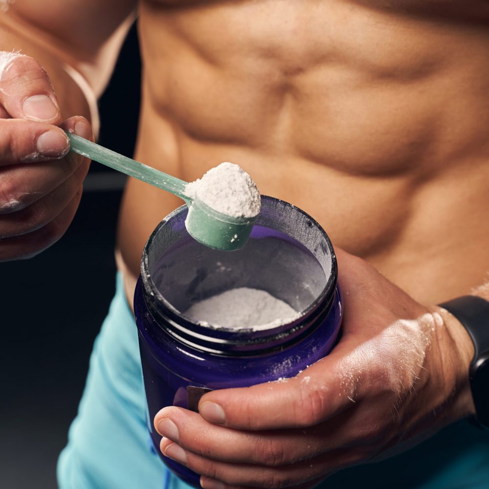 Athletic man holding a container with protein powder Cropped photo of a shirtless muscly man wearing sport shorts and scooping powder protein from a jar