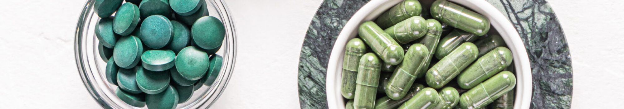 Green spirulina algae powder, capsules and tablets in jars on white embossed background. Vertical view. A copy of the space. Detox. Green spirulina algae powder, capsules and tablets in jars on white embossed background. Vertical view. A copy of the space. Detox